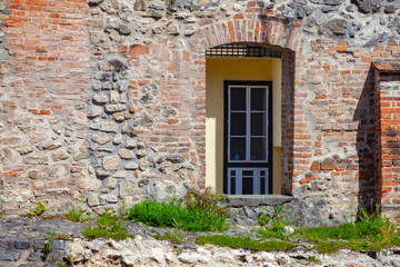 A fragment of an old fortress wall with an opening for a door through which the wall and door of a modern building are visible. A symbol of the connection of the past and the present