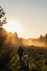 Vintage hunter walks the forest road. Rifle Hunter Silhouetted in Beautiful Sunset or Sunrise. Hunter aiming rifle in forest - 297435155