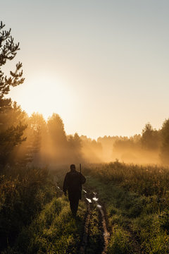 Vintage hunter walks the forest road. Rifle Hunter Silhouetted in Beautiful Sunset or Sunrise. Hunter aiming rifle in forest