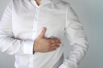 man in a white shirt holds on to the chest in the heart, symbol of problems, pain, illness, first...