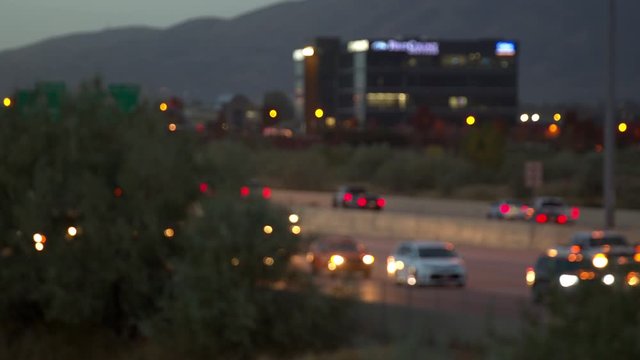 Background traffic moving on highway out of focus in the evening commute with lights on.
