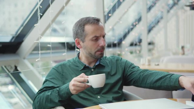 Camera panning left to adult entrepreneur having break in cafe and after receiving message suddenly remembering urgent remark to do in project on laptop looking satisfied with time limit