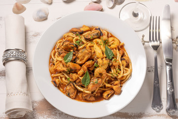 Pasta with sea fruit in white plate on a white wooden background, soft light. Spaghetti ai frutti di mare, seafood mediterranean gastronomy