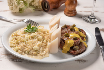 Risotto with filet mignon. Risoto and beef with capers and mustard in a white plate on wooden white background. Soft light. Italian food.
