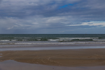 Whangamata, Coromandel peninsula. Single yacht in frame. Calm, quiet day at usually very busy surf beach. Unusual. Murky weather, hazy. Small waves breaking on shore, white sand, beautiful holiday.
