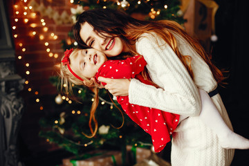 Elegant mother in a white sweater. Little girl near christmas tree