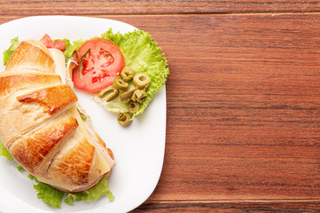 Croissant sandwich with salad, ham, cheese, tomatoes and olives on wooden background. Morning breakfast concept. Healthy and fast food. Isolated.