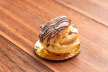 Profiteroles with ice cream and chocolate. Eclairs with black chocolate on wooden background. Traditional French dessert.