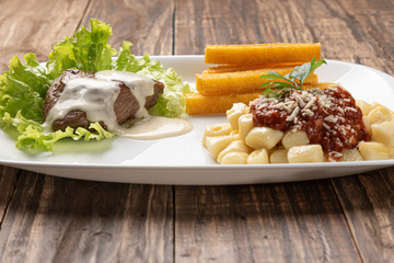 Homemade gnocchi pasta with tomato sauce and beef mignon with cheese sauce in a white plate on wooden  background