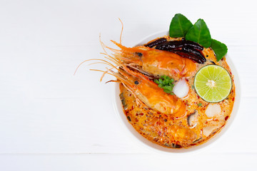 Tom Yum Goong or Shrimp soup spicy sour Soup Traditional food in Thailand contains chili lime ginger galangal lemongrass lime leaf from top view on a white wood background.