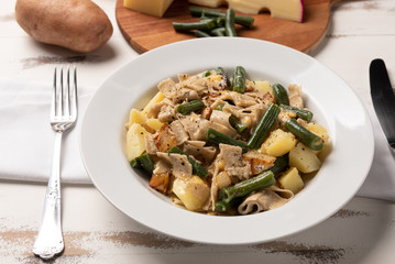 Homemade Pizzoccheri alla valtellinese;  a traditional short tagliatelle pasta typical of northern Italian province of Valtellina. White plate on wooden white  background. Soft light