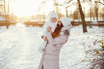 Family have fun in a winter park. Stylish mother in a pink jacket. Little girl in a winter clothes.