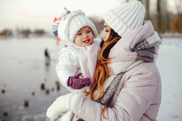 Family have fun in a winter park. Stylish mother in a pink jacket. Little girl in a winter clothes.