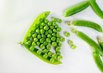 many green pea berries are scattered in front of the pod on a white background