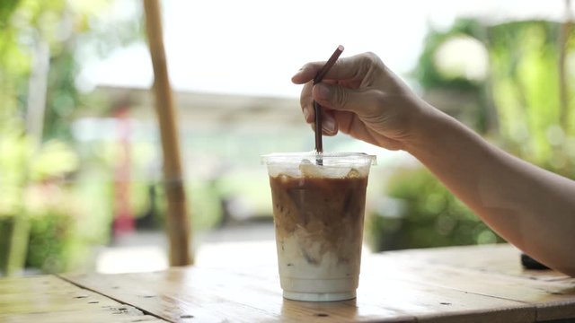 Hand mixing coffee with milk for making iced latte drink with the straw