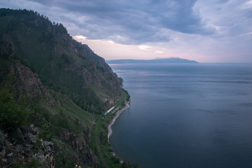 Fototapeta premium View from the mountain to a passing train by rail along Lake Baikal