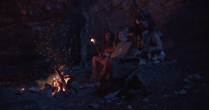 At night tribe cavemen neanderthals wearing animal skin woman use tablet computer sitting by the fire in a cave stone fun male ancient history evolution homo sapiens primitive campfire slow motion