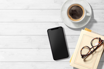 スマートフォン、コーヒー、本のある白木のテーブル