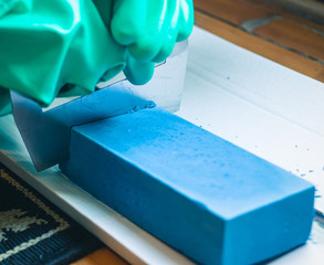 Woman with green gloves cutting an homemade blue soap loaf