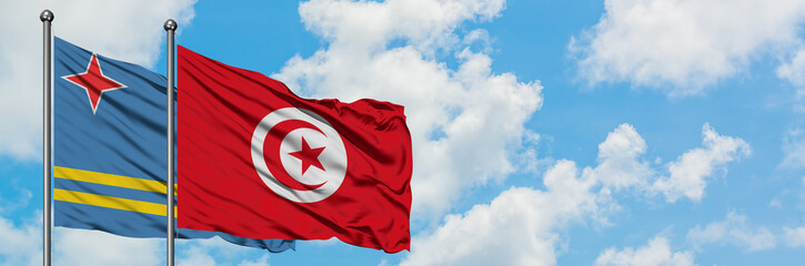 Aruba and Tunisia flag waving in the wind against white cloudy blue sky together. Diplomacy concept, international relations.