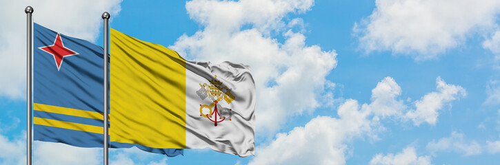 Aruba and Vatican City flag waving in the wind against white cloudy blue sky together. Diplomacy...