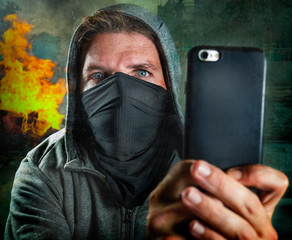 young rioter filming street chaos . ultra and radical man masked recording riot video on mobile phone during violent turmoil witnessing brutality anti system demonstration
