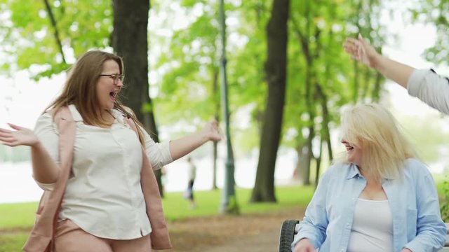 Medium shot of plus size woman walking in park and meeting unexpectedly two girlfriends sitting on bench. Three ecstatic female friends hugging and jumping happily