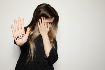 Young woman with word HELP written on her palm against light background, focus on hand. Space for...