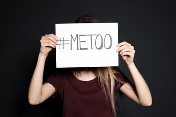 Young woman holding #METOO card against dark background