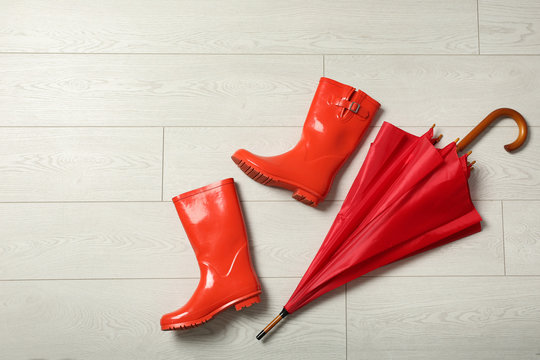 Color umbrella and rubber boots on wooden floor, flat lay. Space for text