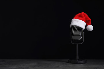 Microphone with Santa hat on grey stone table against black background, space for text. Christmas...