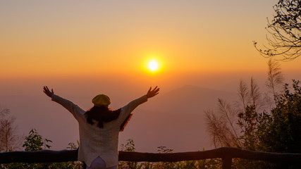 Fototapeta premium Woman tourist is a cheerfully, she is watching sunrise with mist in the morning, orange sky, viewpoint at Phu Ruea National Park, Loei, Thailand.