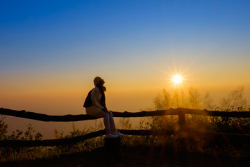 Fototapeta na wymiar Woman tourist is a cheerfully, she is watching sunrise with mist in the morning, orange sky, viewpoint at Phu Ruea National Park, Loei, Thailand.
