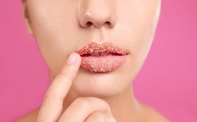 Young woman with sugar scrub on lips against pink background, closeup