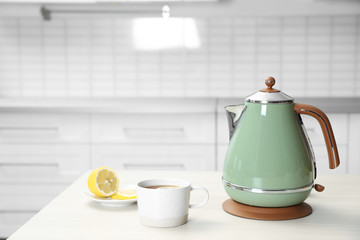 Modern electric kettle, cup of tea and lemon on wooden table in kitchen