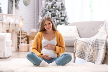 Young pregnant woman sitting on floor in room decorated for Christmas - Powered by Adobe