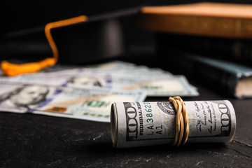 Dollar banknotes, student graduation hat and books on black table. Tuition fees concept