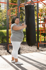 Beautiful overweight woman kicking heavy bag on sports ground