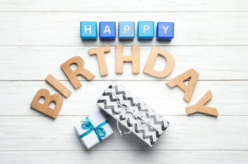 Flat lay composition with words HAPPY BIRTHDAY and gift boxes on white wooden background