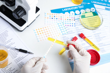Fototapeta premium Doctor holding test tube with urine sample for analysis at white table, top view