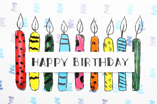 Card with words HAPPY BIRTHDAY and colorful drawn candles on paper sheet, top view