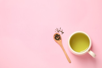 Spoon with green tea leaves and cup of hot beverage on pink background, flat lay. Space for text
