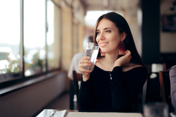 Thirsty Woman Drinking a Glass of Water in a Restaurant