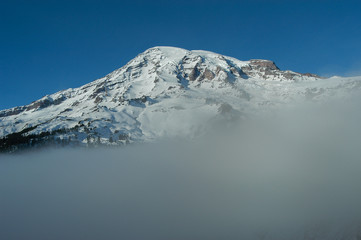 Fototapeta na wymiar Snow-capped peak of Mt. Rainier rising above the fog layer against a clear sky in Mt. Rainier National Park, Washington State, USA.