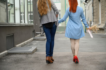 Same-sex relationships. Happy lesbian couple walking down the street holding hands. The backs of two beautiful women on a date with a bouquet of dried flowers. LGBT.