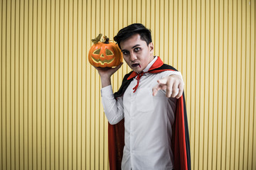 Young Asian man in costume Dracula on yellow background.