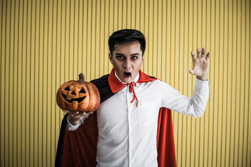 Young Asian man in costume dracula on yellow background.