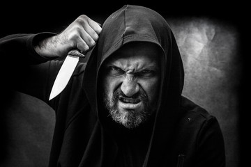 Black and white portrait of a bald bearded man in a hood on a dirty gray background. Maniac with a knife concept.