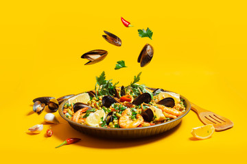 pan with spanish paella with seafood on a yellow background - obrazy, fototapety, plakaty
