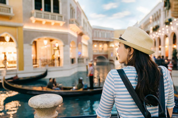 back view of elegant woman traveler with sunhat enjoy view to canal with passing by gondola in las vegas famous hotel. young girl backpacker smiling looking boat during sunset outdoors on summer trip © PR Image Factory
